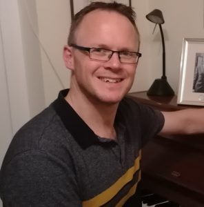 Person sitting at a piano, smiling to the camera.