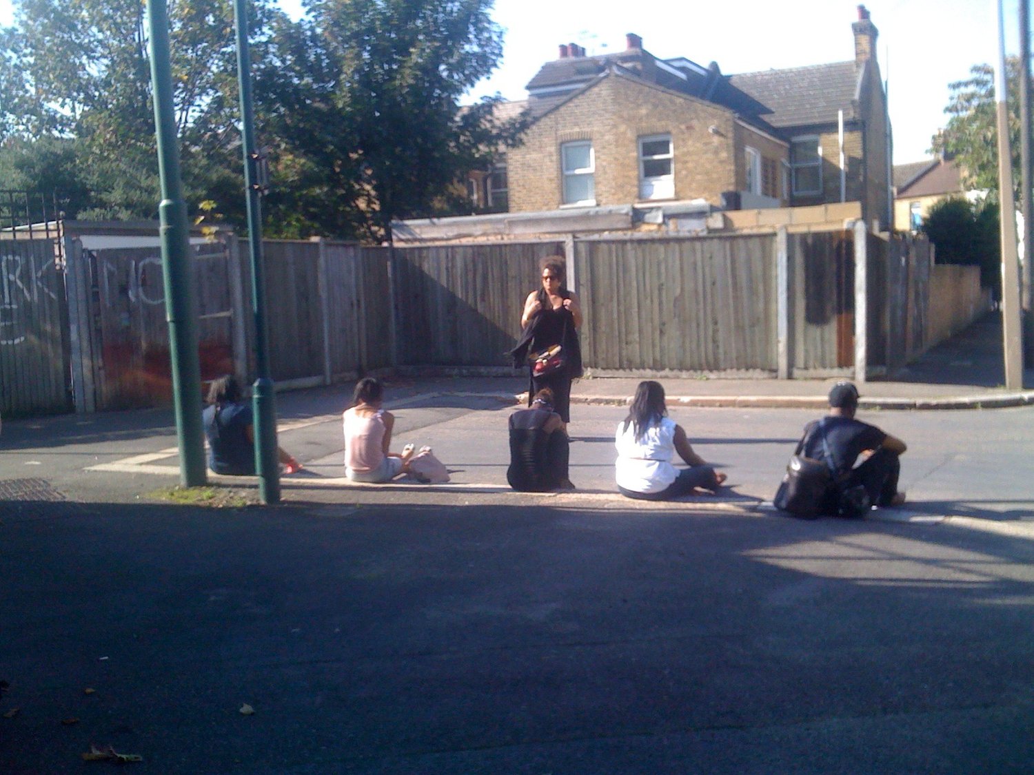 Woman talking to group of young people sitting on the ground outside.