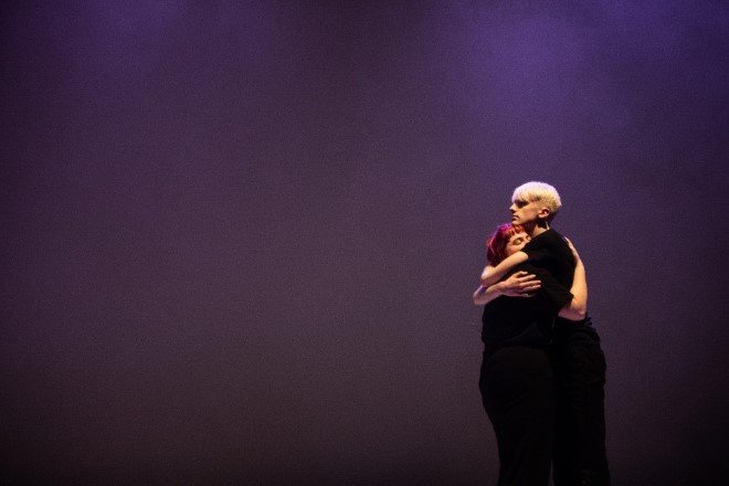 Two actors embracing on stage from afar.