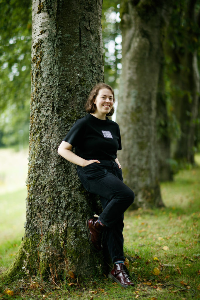 Young woman smiling and leaning against a tree in a wood.