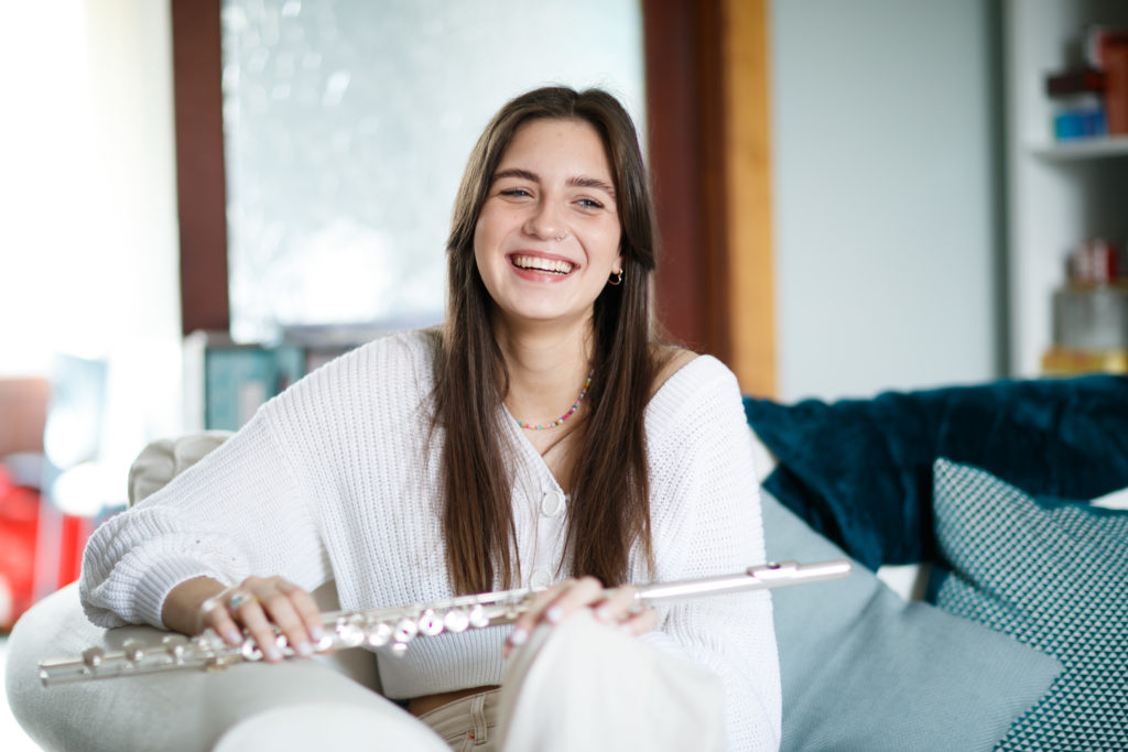 Young woman sitting on a sofa, smiling with a flute on her lap.