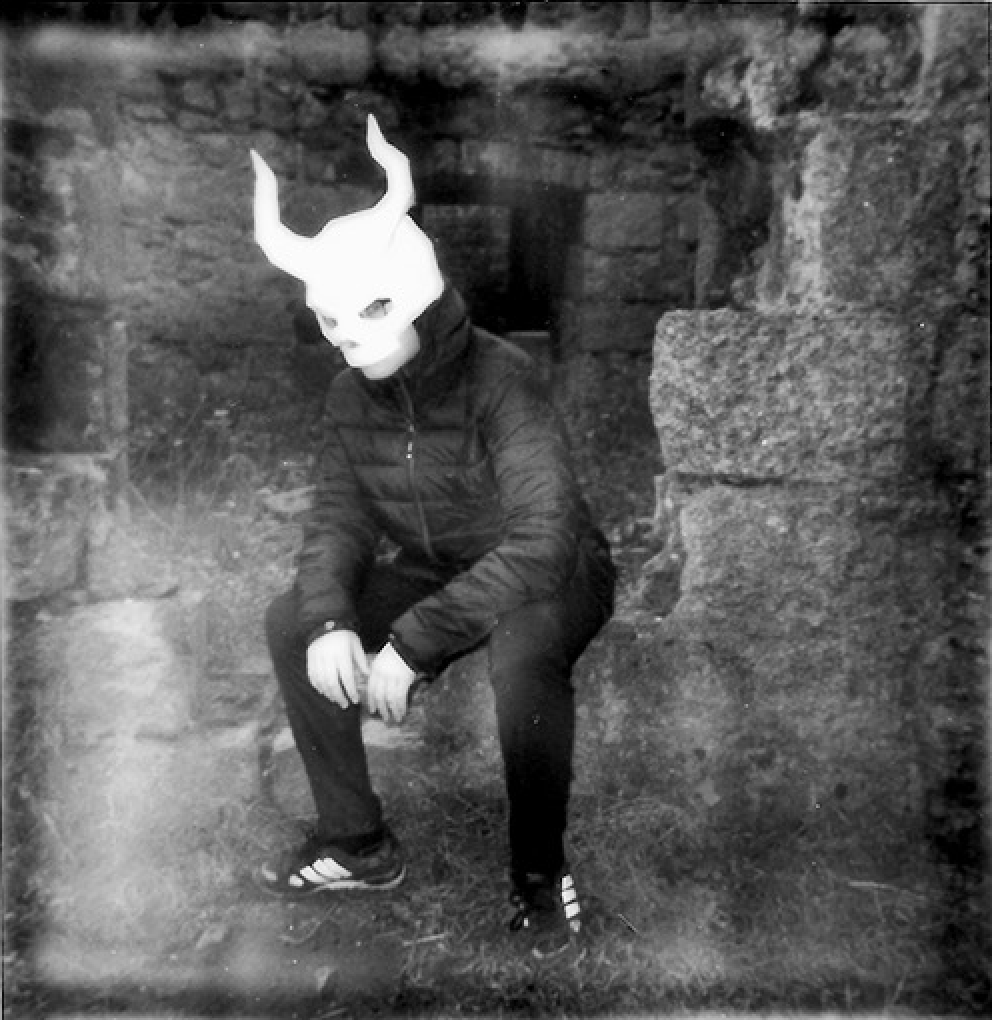 Person wearing a horned mask sitting on a castle wall.