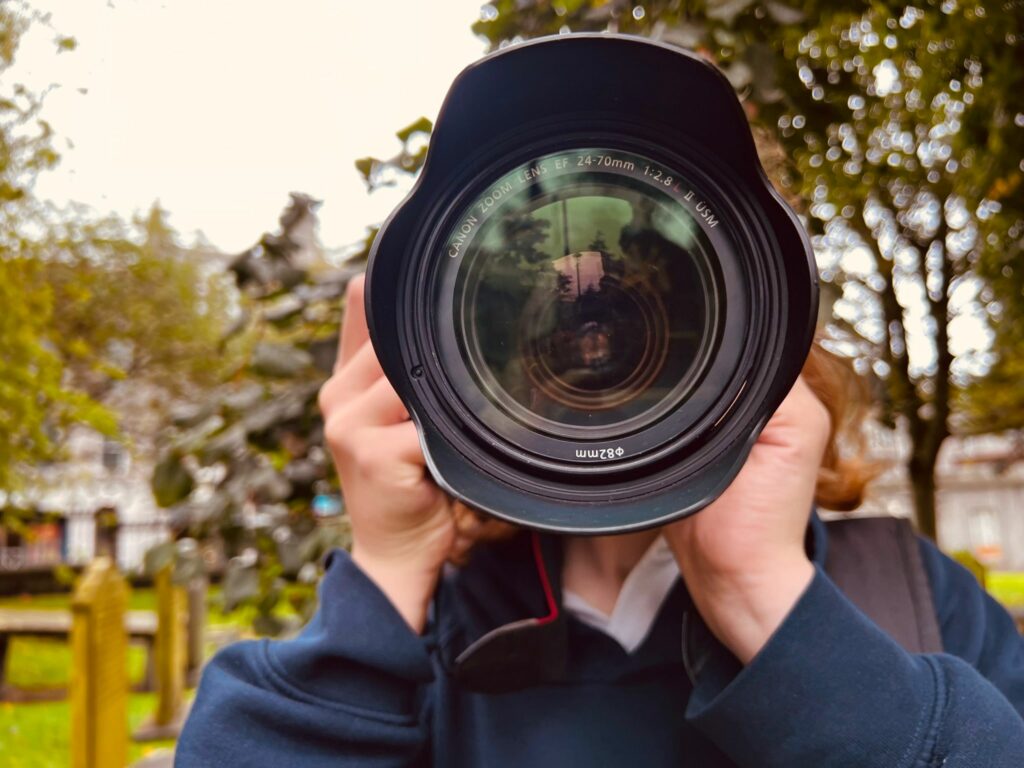 Young person holding a camera hiding their face