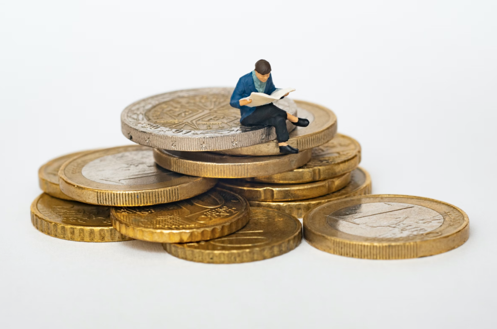 A stack of coins with a tiny model person sitting on top of them