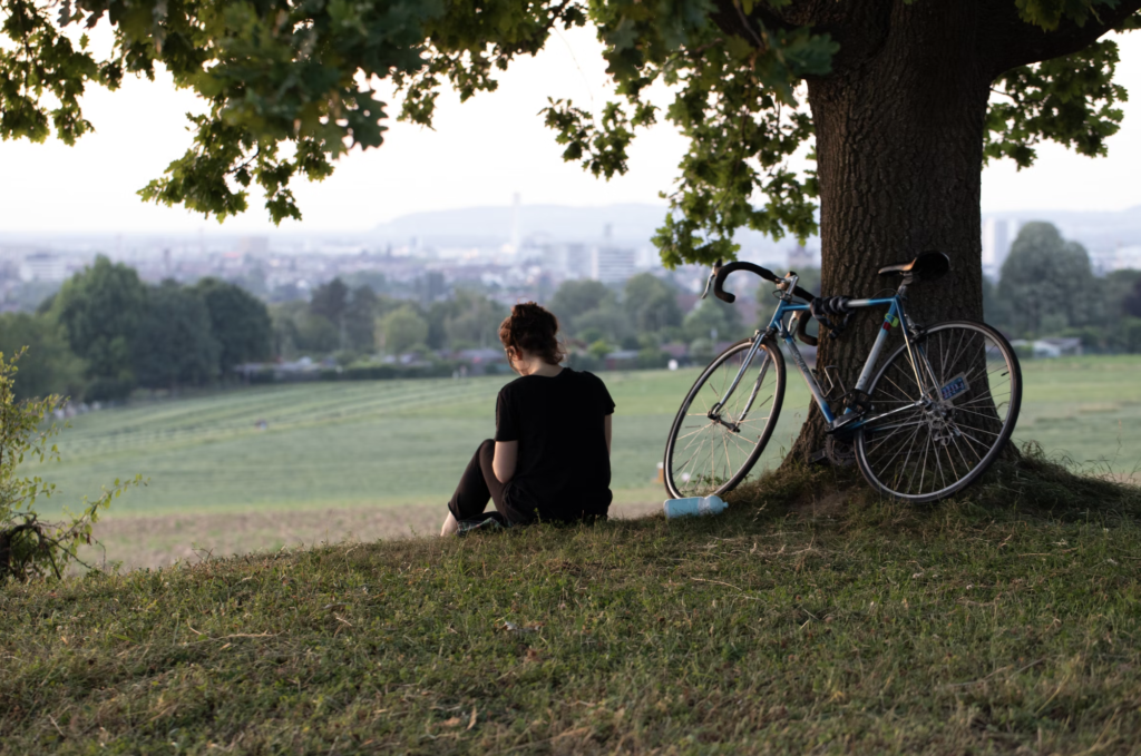 Woman sitting reading under a tree next to her bike