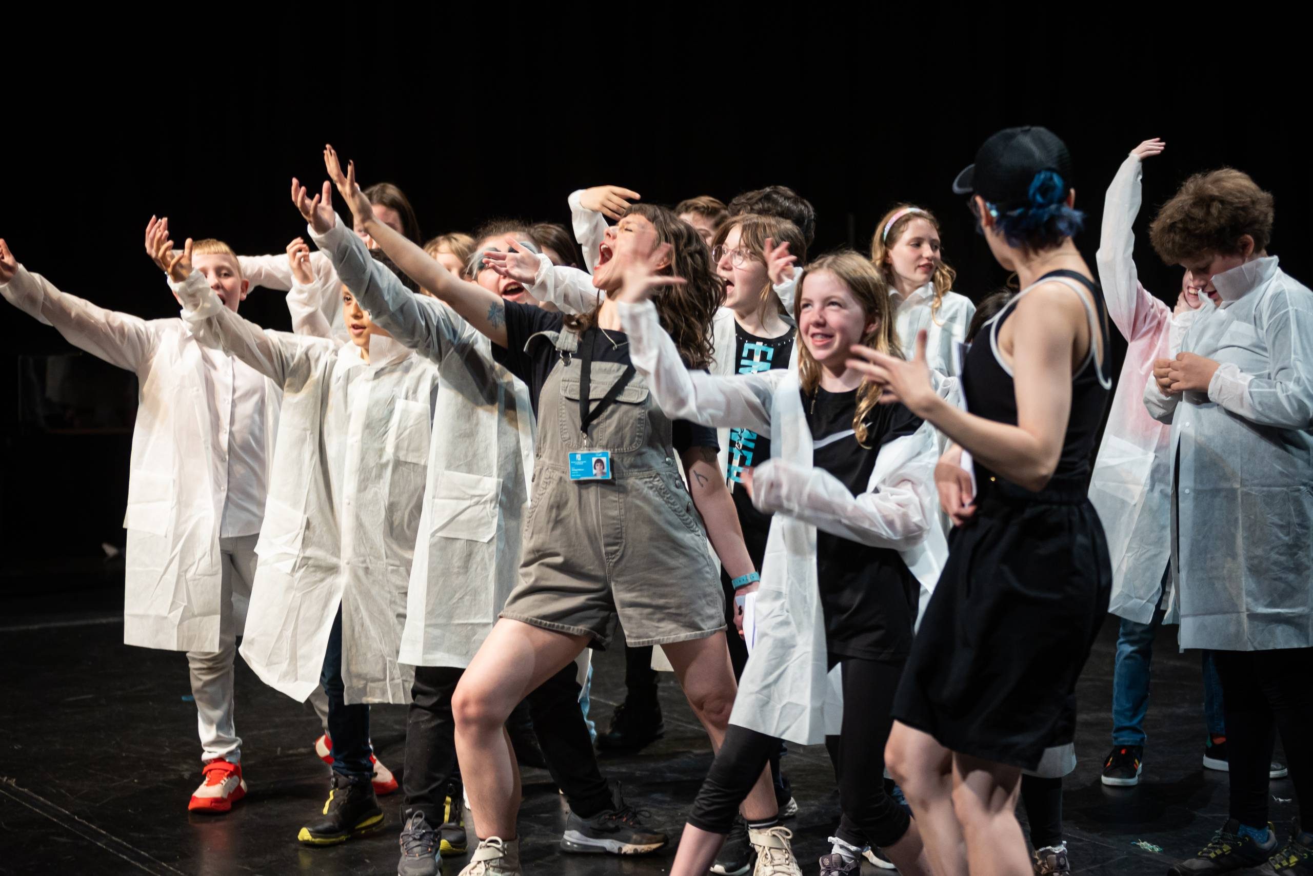 A group of young people with a tutor, all wearing doctor jackets and rehearsing a play