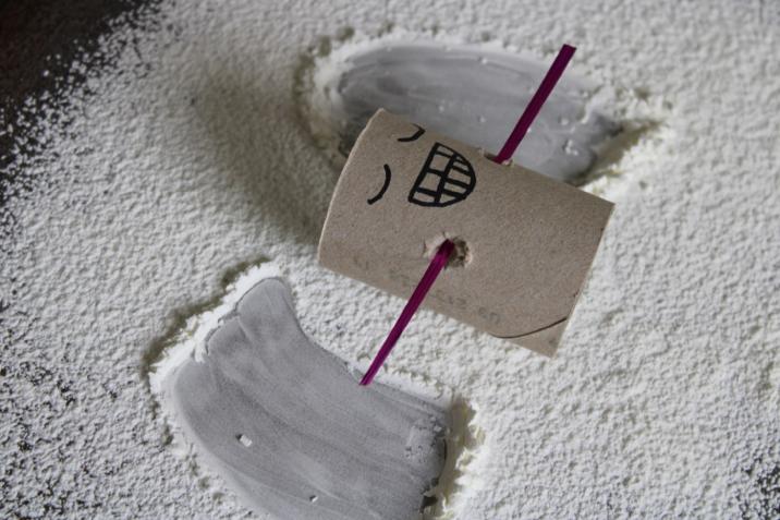 Cardboard toilet roll holder with faces drawn on lying down making a snow angel in flour