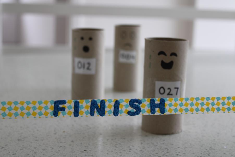 Cardboard toilet roll holder with faces drawn on reaching a finish line