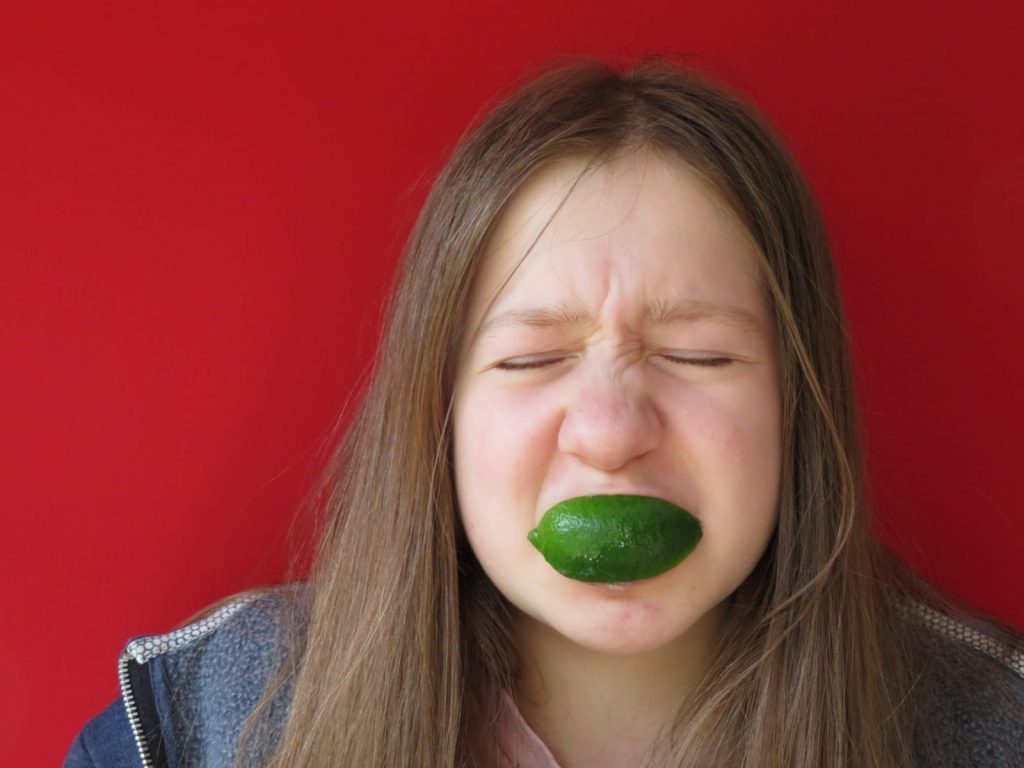 Girls with sour lime wedge in mouth,