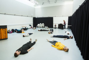 Seven young people in a drama studio lying on the floor