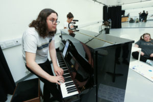 Young person with glasses standing and playing the piano